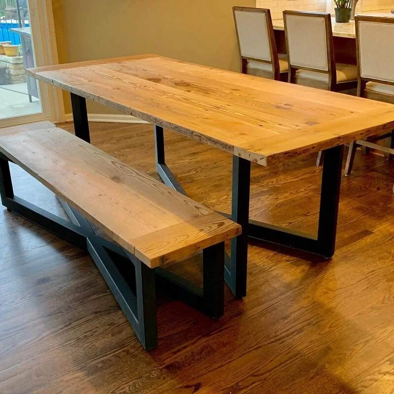 A handcrafted wooden table with a rich, natural finish, featuring a live edge design and sturdy black metal legs. The table is set in a well-lit indoor space with a neutral-toned background, highlighting the wood grain and craftsmanship.