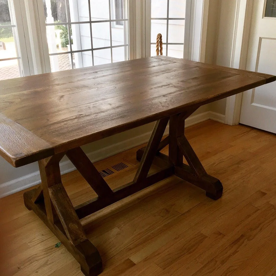 Rectangular wooden table with X-shaped legs, photographed against a dark studio wall.