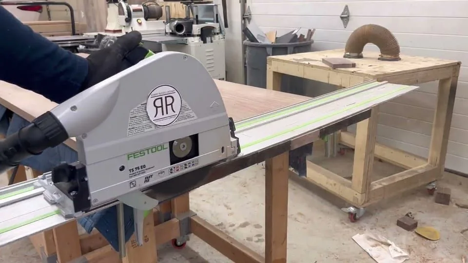 A plunge saw running along its guide rail down the length of a board on the bench.