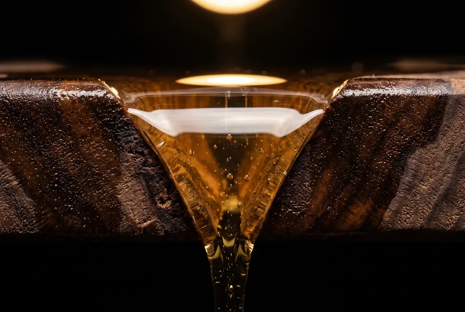 Clear amber resin flowing into the channel between two dark walnut edges, fine bubbles suspended in it.