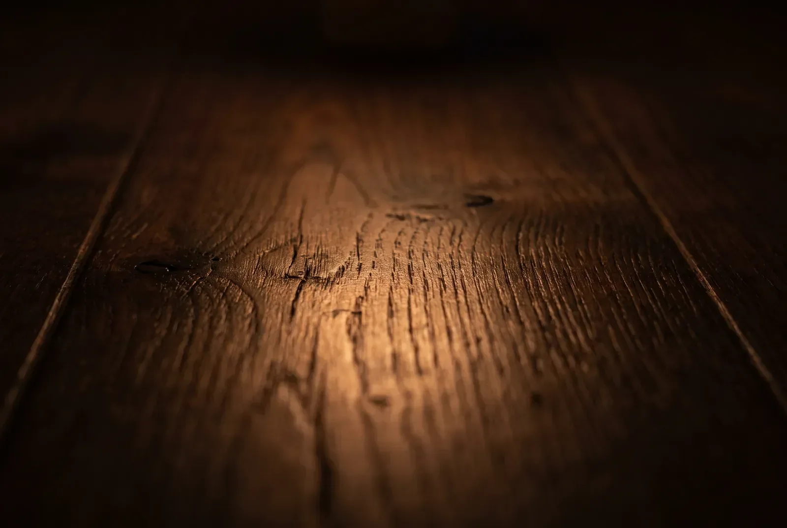 Warm candlelight pooling low across a bare oiled hardwood surface, the grain in long relief.