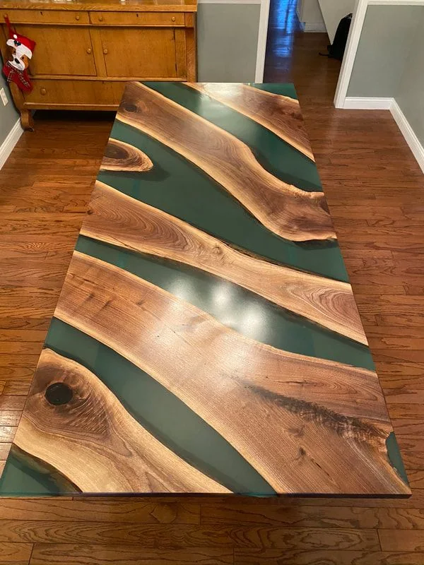 Wood and green resin table with wavy design on wood floor in rustic room.