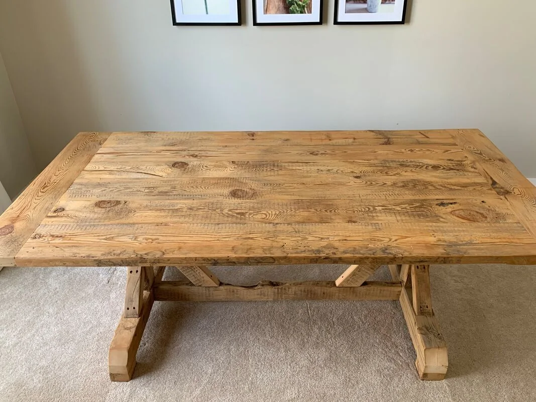 Rustic wooden table with a rectangular top and cross-braced legs, photographed against a dark studio wall.