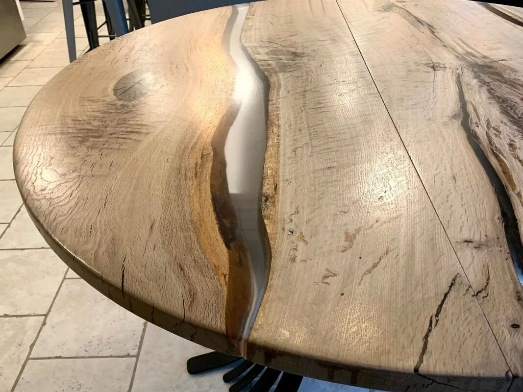 Close-up of a custom wooden table with a glossy epoxy resin river design and natural wood grain, set indoors on a tiled floor.