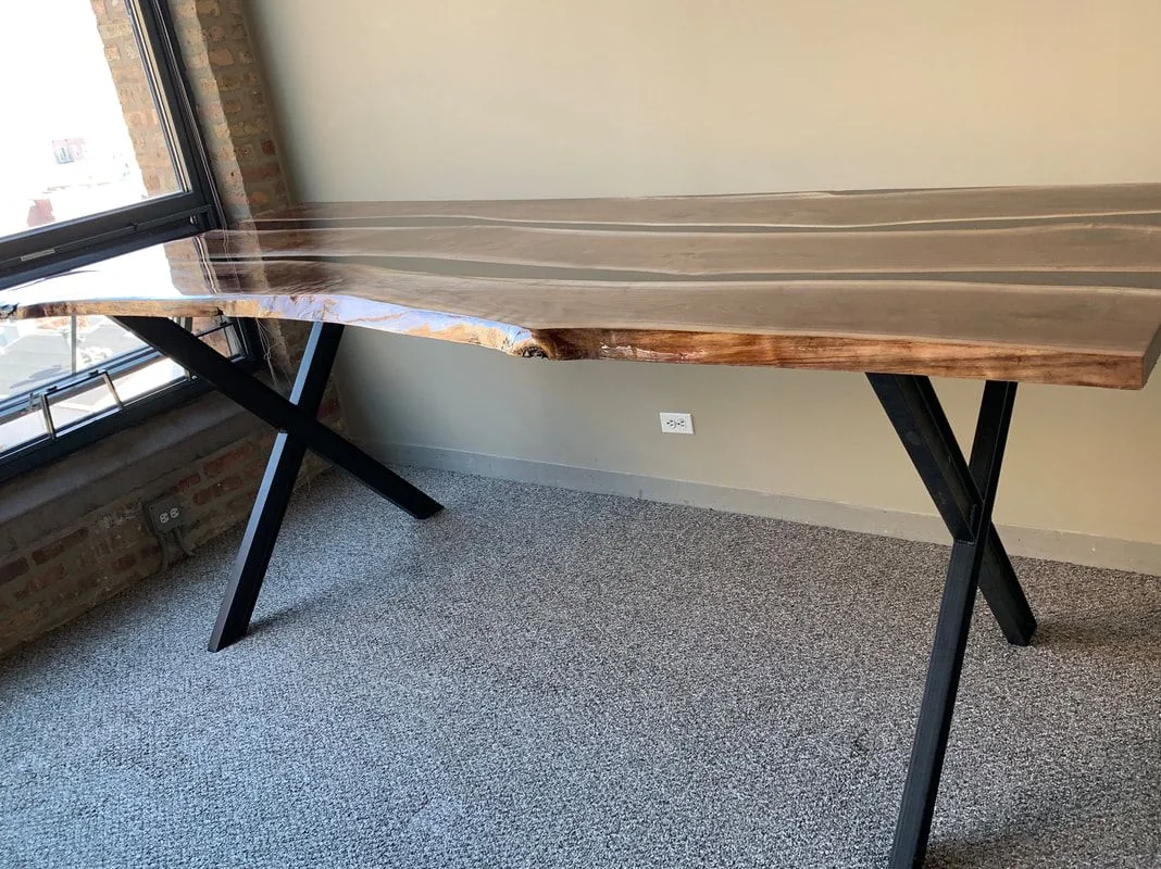 Live edge wood table with glossy finish and black X-shaped metal legs near window.