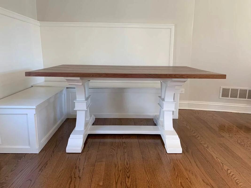 Rectangular wooden table with white pedestal legs, photographed against a dark studio wall.