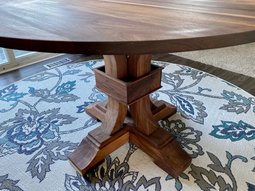 Close-up of a round wooden table base with a dark finish and four curved legs on a floral-patterned rug.