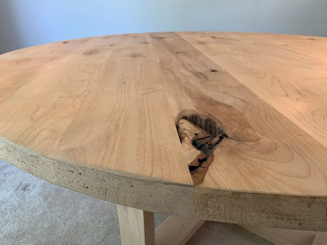 Close-up of round wood table with natural grain and knot detail, smooth edges, and sturdy legs.
