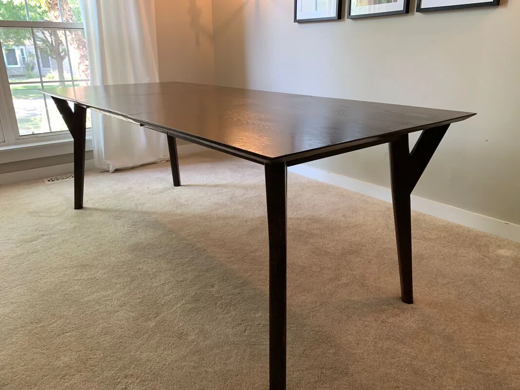 Dark-finished wooden table with angular legs, photographed against a dark studio wall.