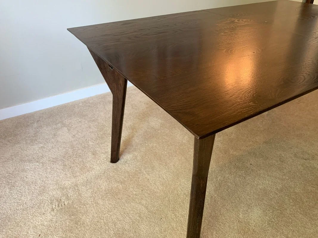 Dark-finished rectangular wooden table with corner-positioned legs, photographed against a dark studio wall.