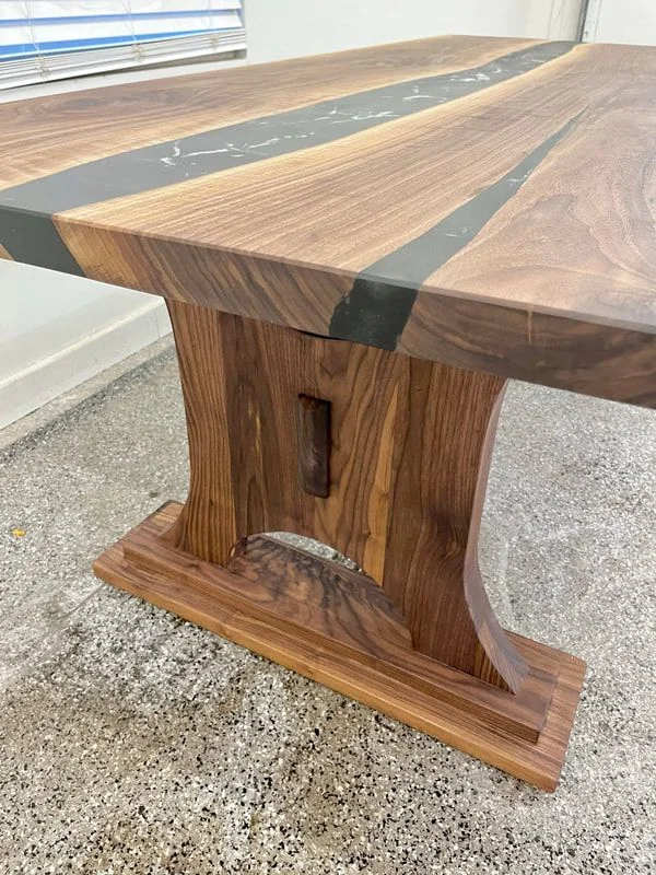 Wooden table with natural grain and two dark resin inlays, featuring a sturdy base with curved supports and detailed craftsmanship.