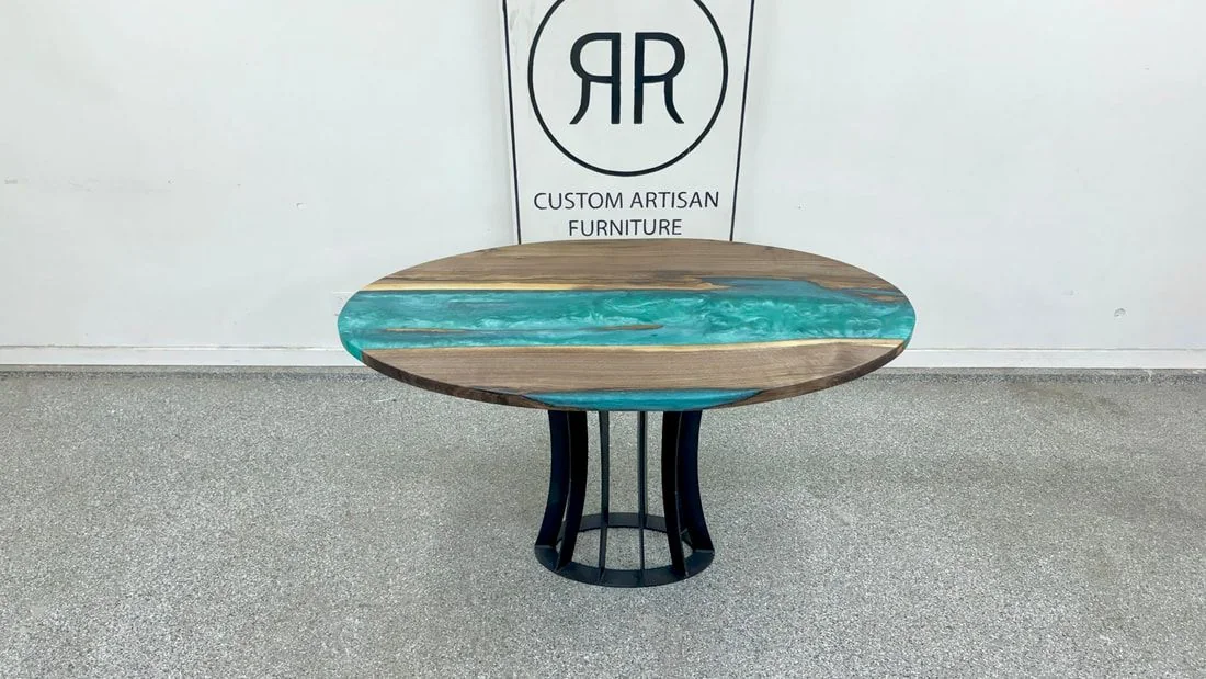 A round walnut table with a turquoise resin river across its center, on a black slatted drum base, photographed against a dark studio wall.