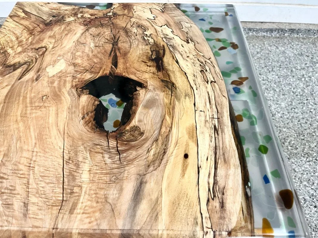 Close view of a spalted maple top with an open natural void, beside a resin band embedded with fragments of colored sea glass.