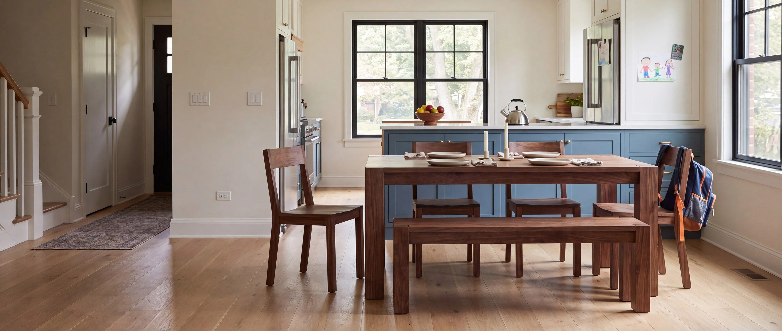 A rendering of a solid walnut dining table with a matching bench, one of Rob's pieces, in a sunny eat-in kitchen, set for dinner.