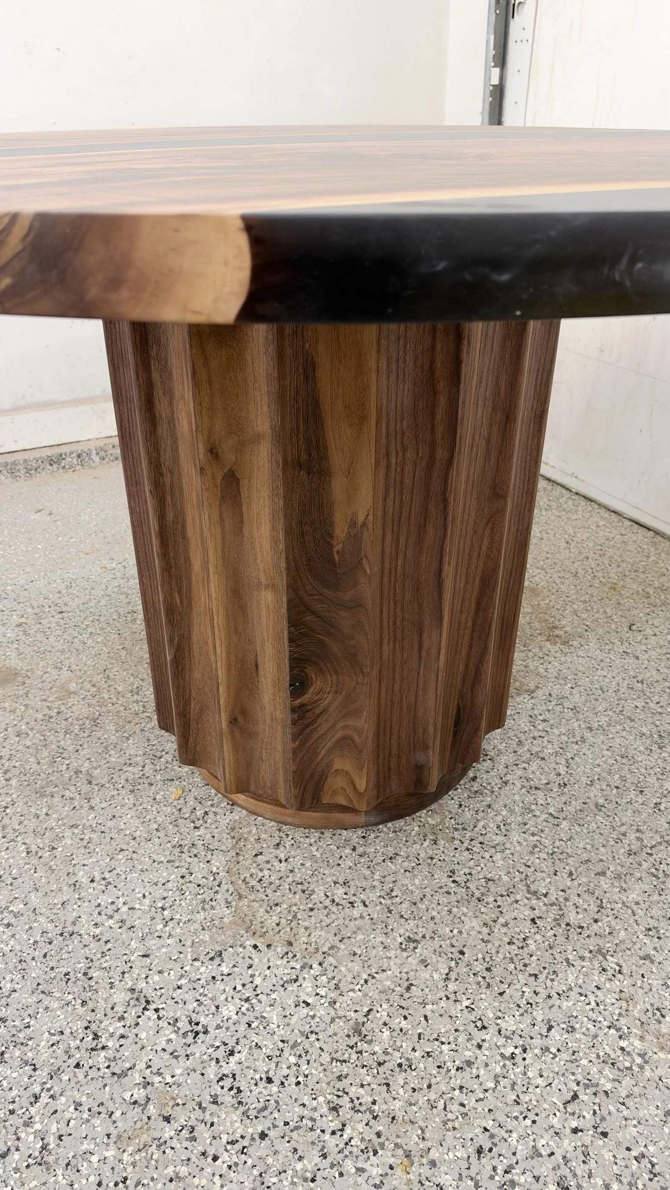 Close view of the fluted wood drum pedestal under the round top, with the black resin showing at the edge of the top.