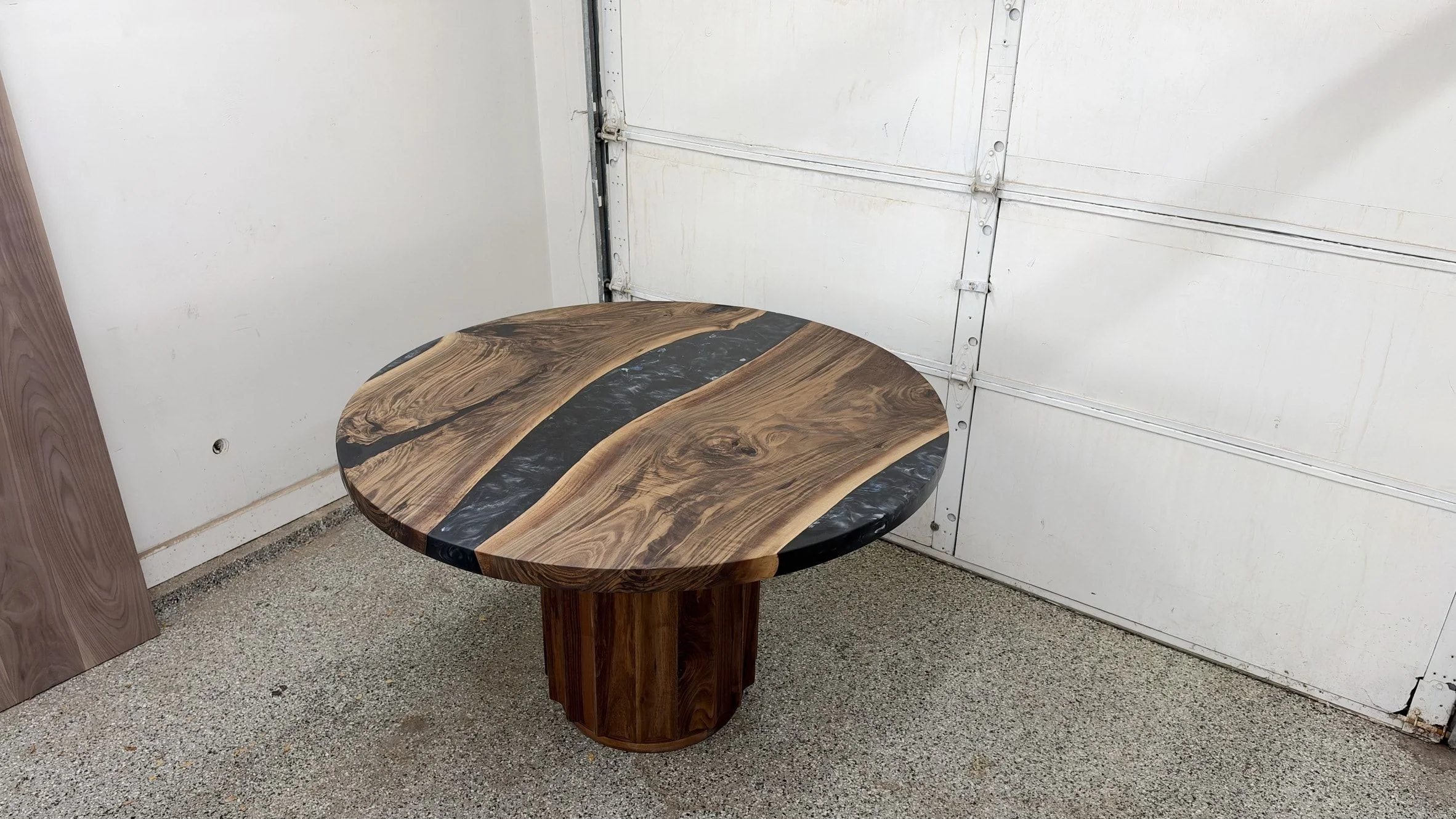 The same round table from across the studio: two live edge boards either side of a black resin river, on a fluted pedestal.