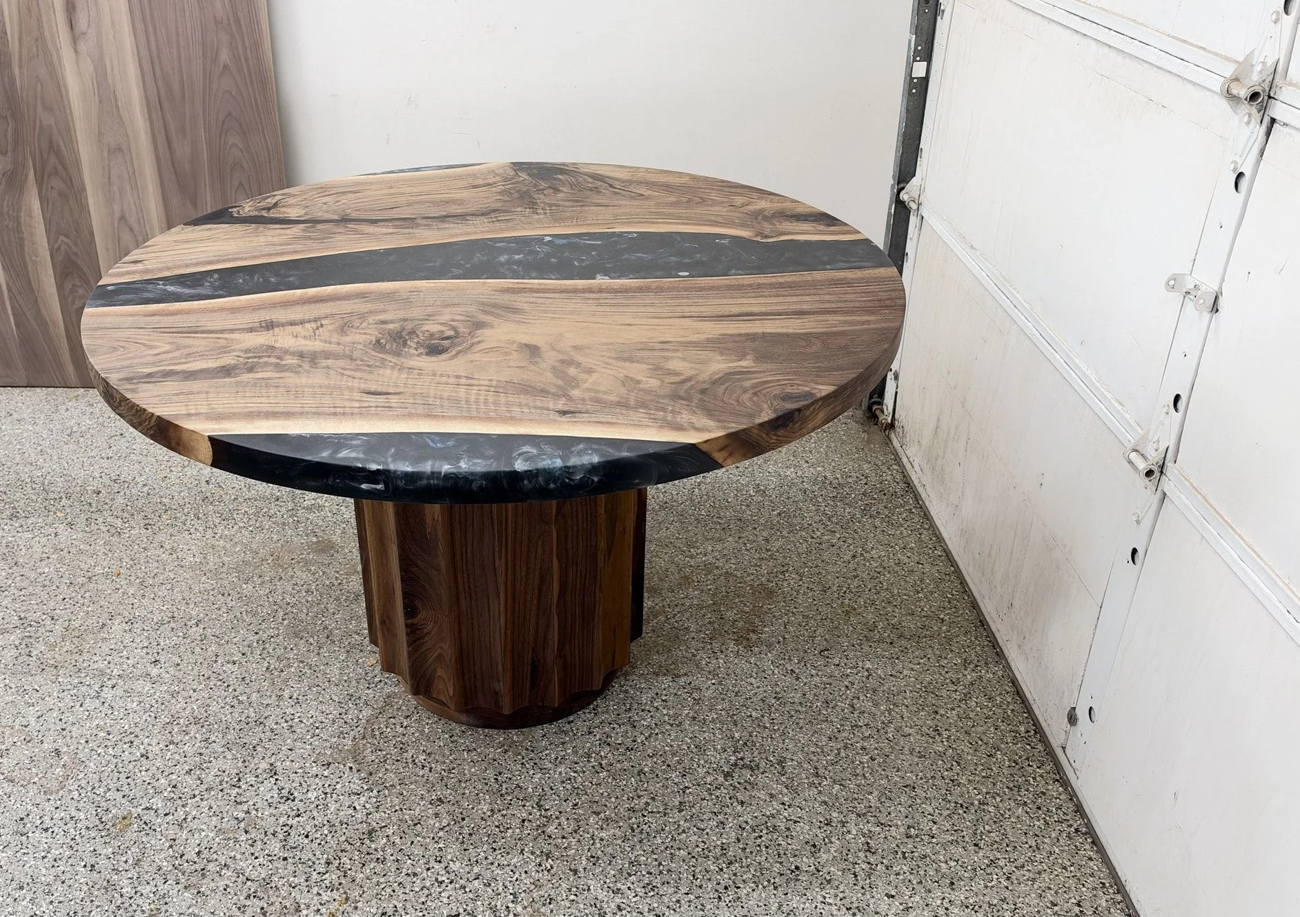 Round table with a black resin river between two walnut boards, seen from above at an angle, on a fluted drum pedestal.