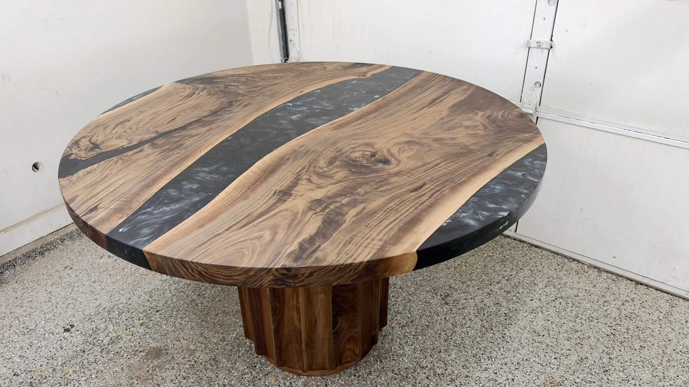 Round live edge table with a wide black resin river across the top, on a fluted wood drum pedestal, photographed in the studio.