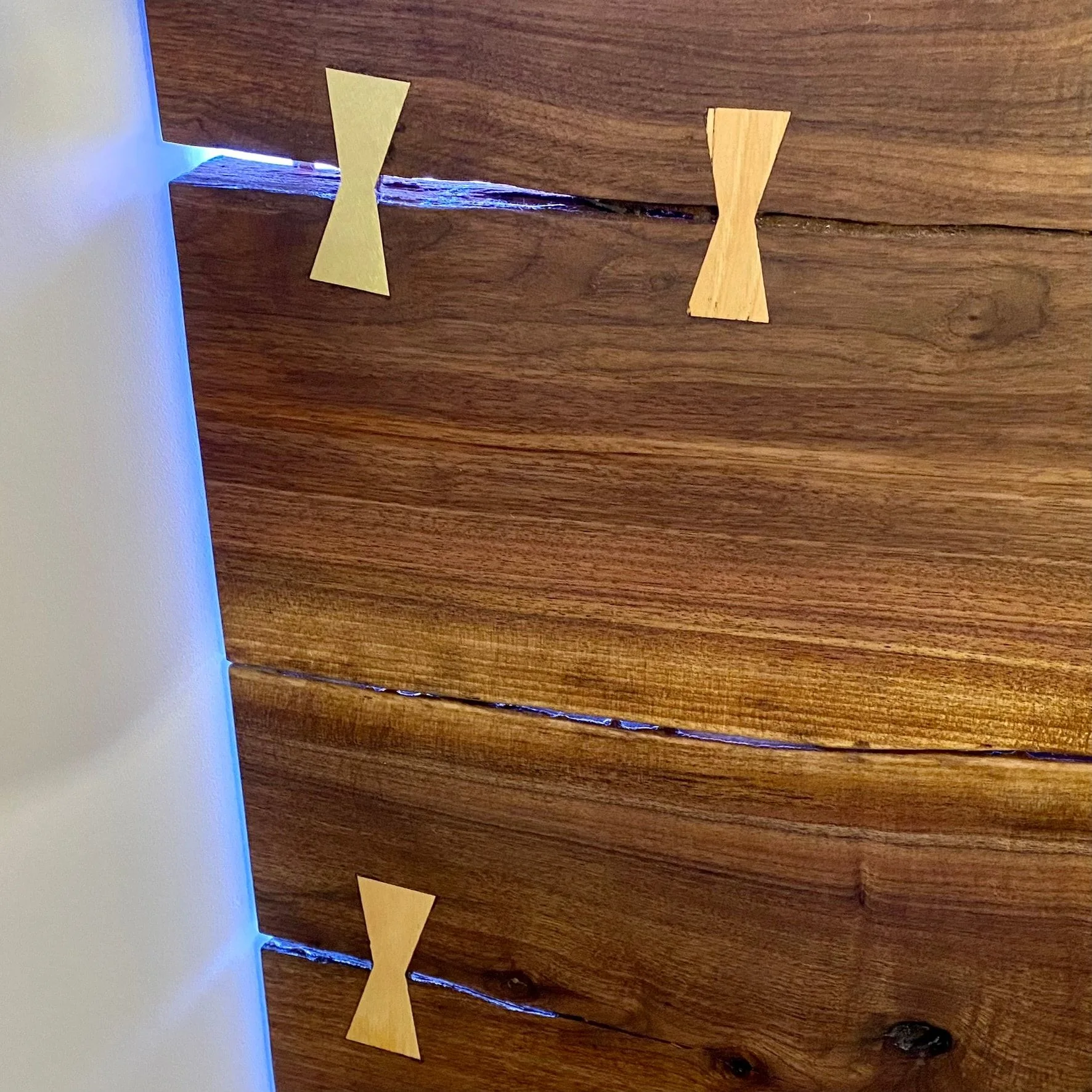 Close view of pale bowtie keys set across open seams in a dark slab, with light showing through the seams.