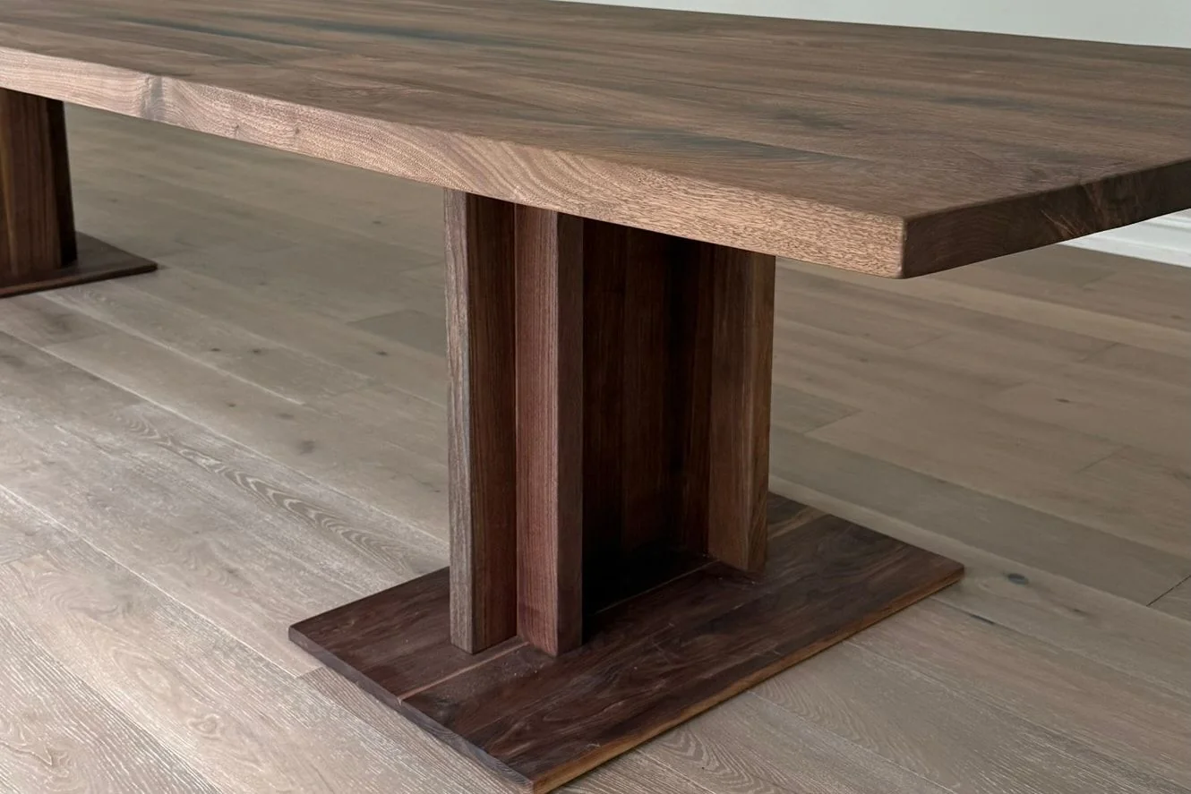 The same pedestal built in walnut under a long walnut top, standing on its rectangular plinth on a pale oak floor.
