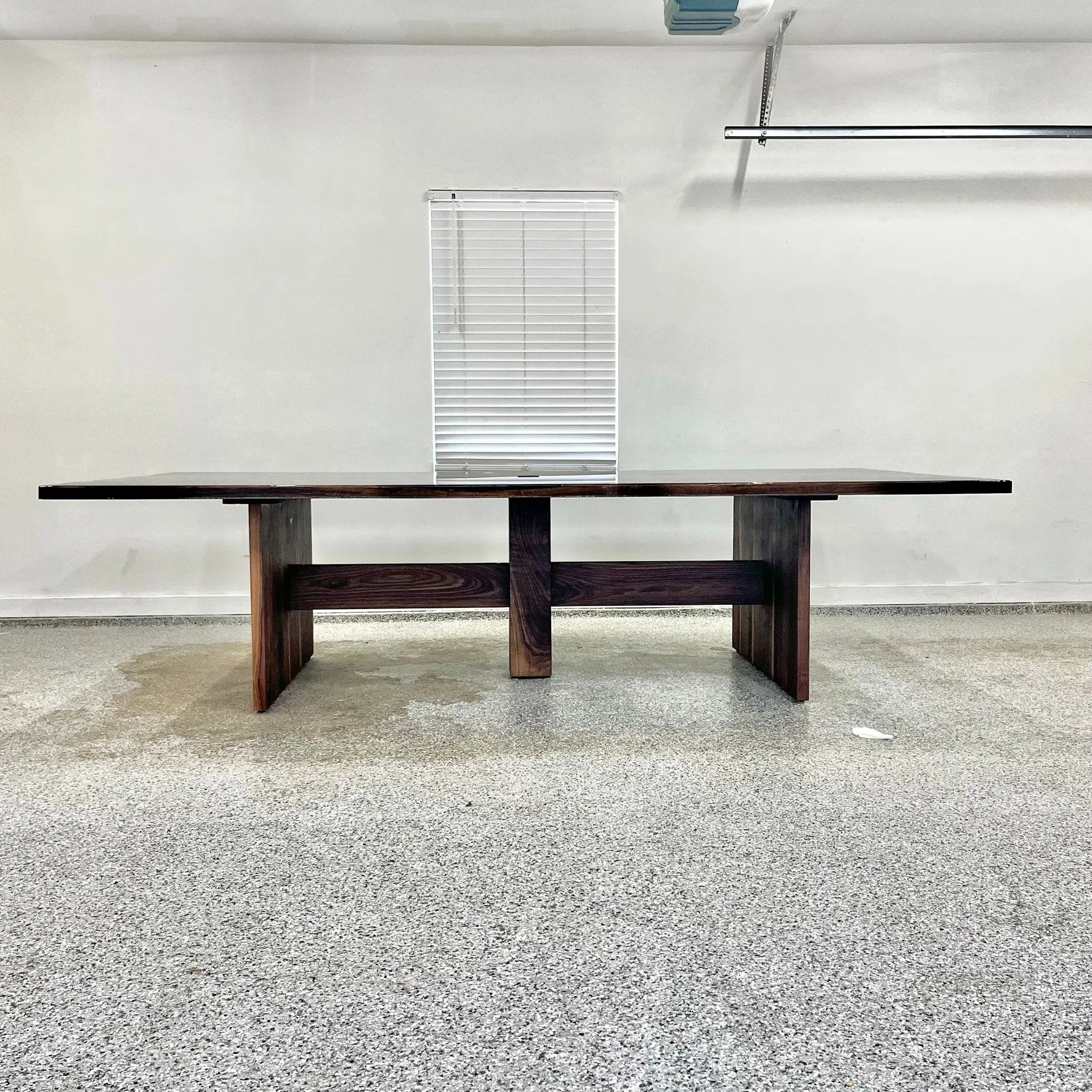 The walnut conference table seen from the side, showing the slab legs, a center support and the stretcher.