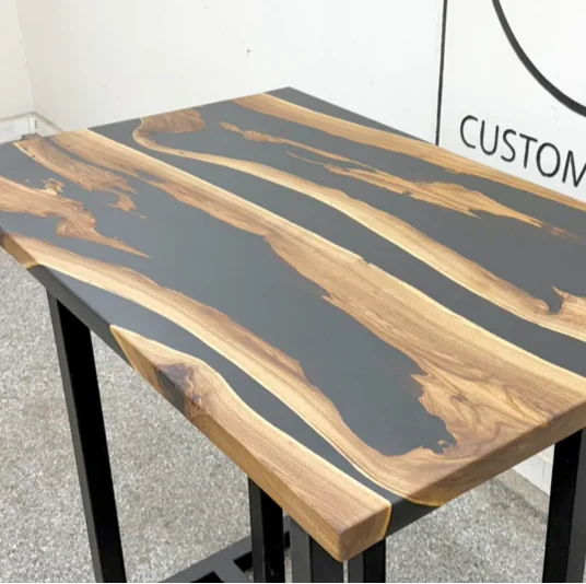 Custom live edge dining table with black resin river and modern metal legs, photographed against a dark studio wall.