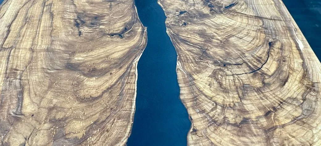 Two bookmatched walnut slabs with heavily figured grain, laid either side of a deep blue resin river.