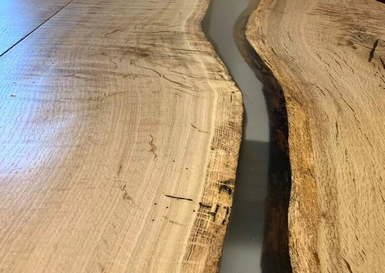 Close-up of a handcrafted wooden table with a flowing resin river design and natural wood grain pattern, photographed against a dark studio wall.