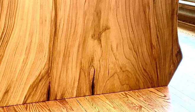 Vertical polished wood slab with natural grain and rustic shape, photographed against a dark studio wall.
