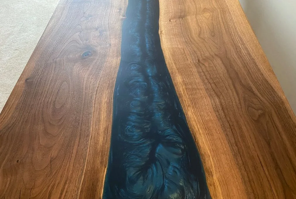 A wooden table with two natural-edge slabs joined by a dark blue resin river featuring swirling patterns, creating an artistic centerpiece.
