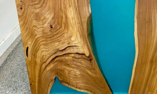 A waterfall-edge cube table in pale elm, a bright blue resin river running across the top and down the side, in the workshop.